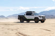 DV8 Offroad Tacoma driving on a desert road with mountains in the background.