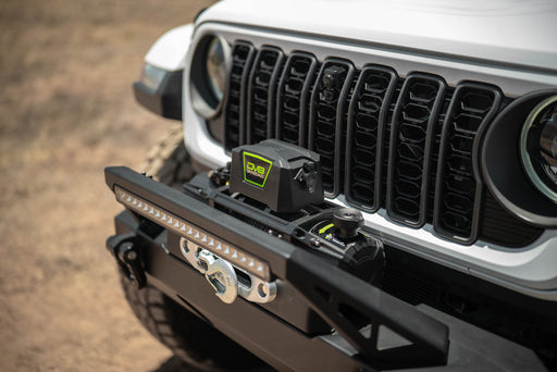 Close-up of a Jeep front bumper with DV8 Xtract 12k Synthetic Rope Winch on a blurred natural background